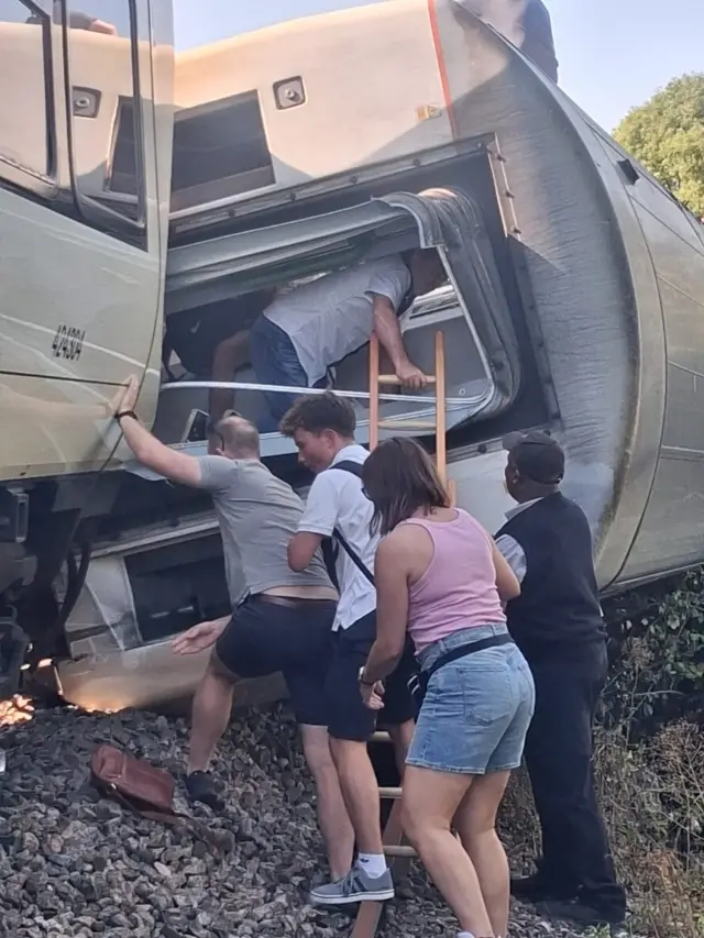 People attempt to leave a train that has derailed.