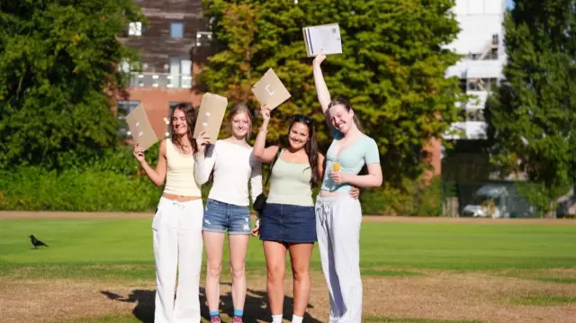 Four students stand and hold their results in the air
