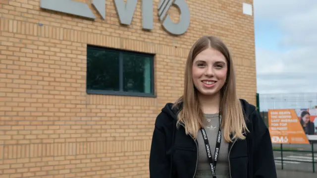 Anastasiia Sochka smiles outside her school. She is wearing a student lanyard