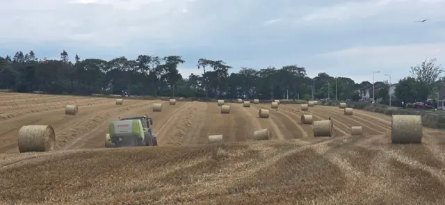 A tractor in a field full of hay in Scotland with cloudy skies