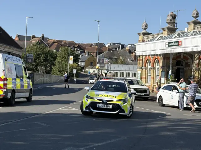 Two police cars outside a railway station, with taxis parked nearby