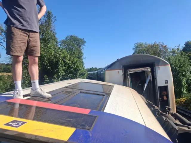 A man stood on top of a tipped over train carriage.