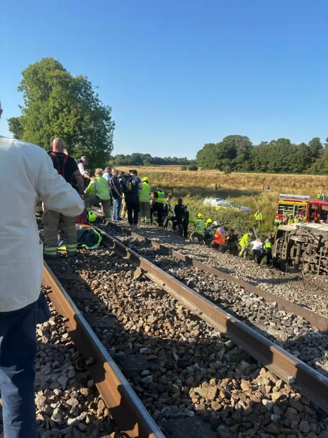 A number of emergency service crews by the side of a train track.