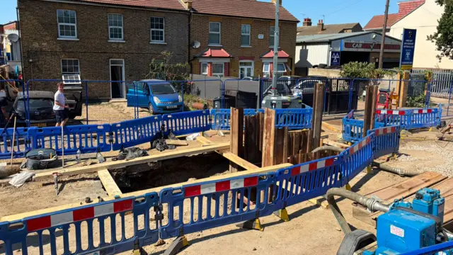 Roadworks shows hole in ground and red/white/blue fences around it
