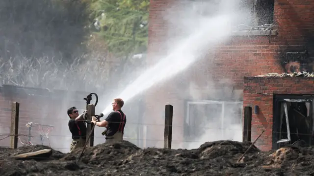 Two firefighters hold a fire hose, which is spraying water at a house that has been badly damaged by a fire.
