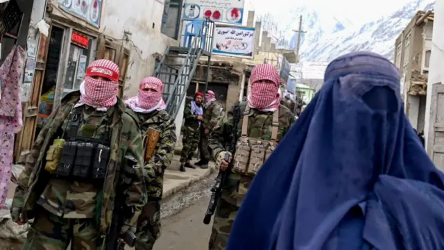 Taliban security personnel stand guard as an Afghan burqa-clad woman (R) walks along a street at a market in the Baharak district of Badakhshan province on February 26, 2024.