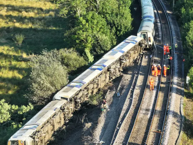 A train lies partially on its side on tracks after derailing