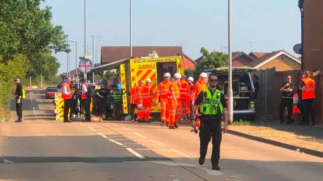 Railway workers in hi-vis, police officers and an ambulance all in a residential road in Wickford. The railway line is pictured out of shot behind some trees to the left.