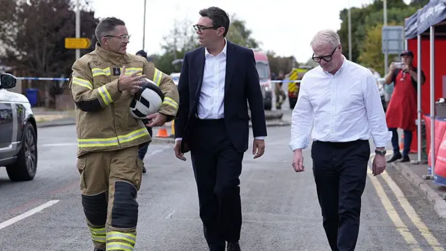 Andy Burnham (C) walks with West Midlands Mayor Richard Parker (R) as he talks to Chief Fire Officer Simon Tuhill