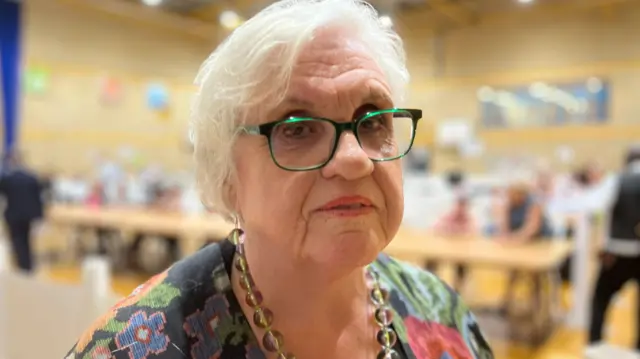 Clacton candidate Pamela Walford wearing green spectacles and wearing a floral top looking toward the camera