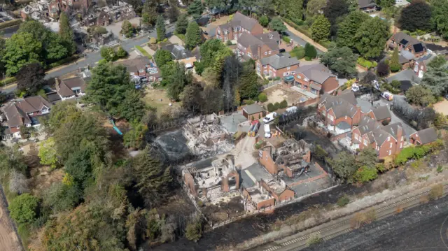 An aerial drone shot of houses affected by the fire. They are burnt to the ground with rubble and black soot everywhere
