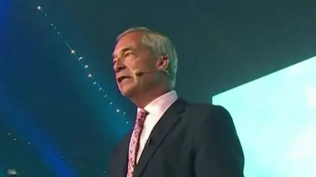 Nigel Farage gives a speech wearing a suit and pink tie