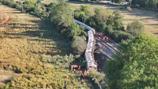 A train lies partially on its side on track after derailing