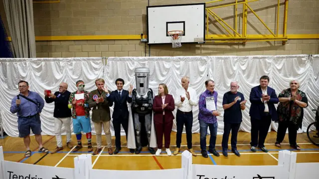 A wide shot of the candidates in the sports hall. Farage is not among them.
