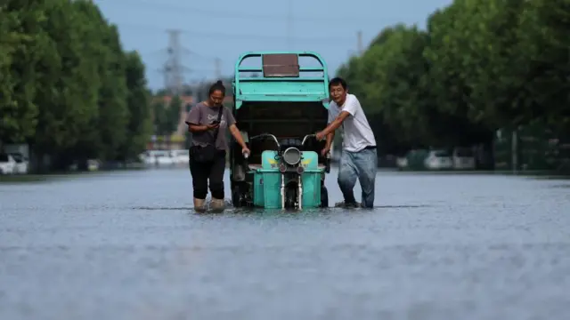 Residents push a vehicle as they wade through a flooded street, following heavy rainfall brought by remnants of Typhoon Dolphin, in Xuchang, Henan province