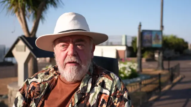 Rick Tracey is pictured wearing a hat and colourful shirt