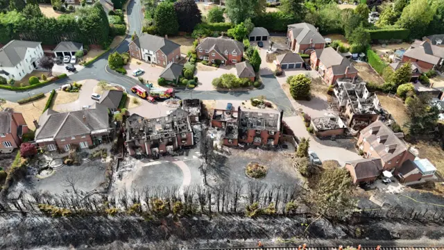 An aerial picture of three homes completely destroyed by fire with no roofs, and scorched earth around them and other houses