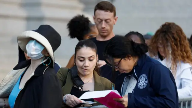 A member of the public presents her ID in line outside court