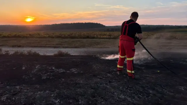 Firefighter with hose at sunset.