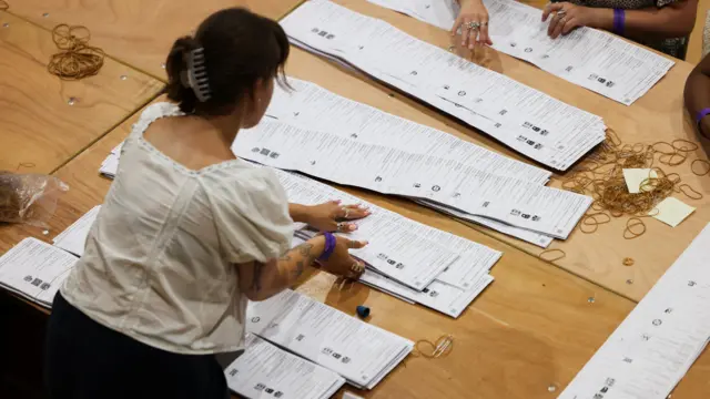 A woman leans over vote papers at a table