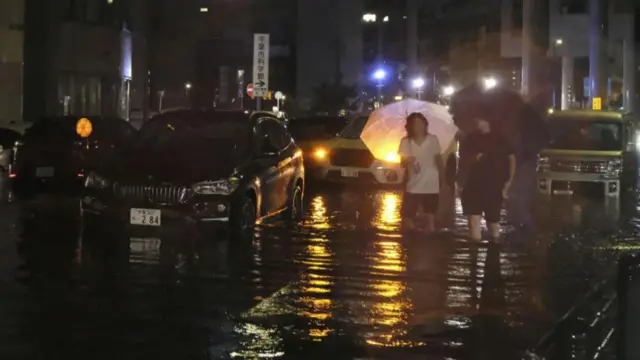 People walk on a flooded road after torrential rain in Chiba