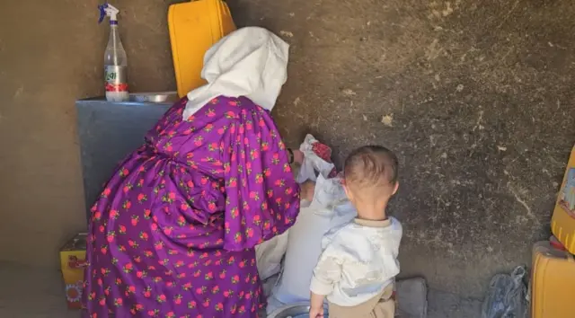 A woman and child from behind, kneeling down while picking something up from the floor