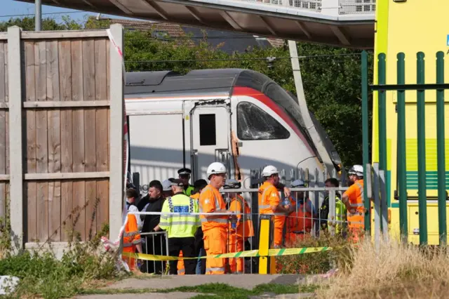 Railworkers and police stand next to a partially derailed train in Wickford, Essex