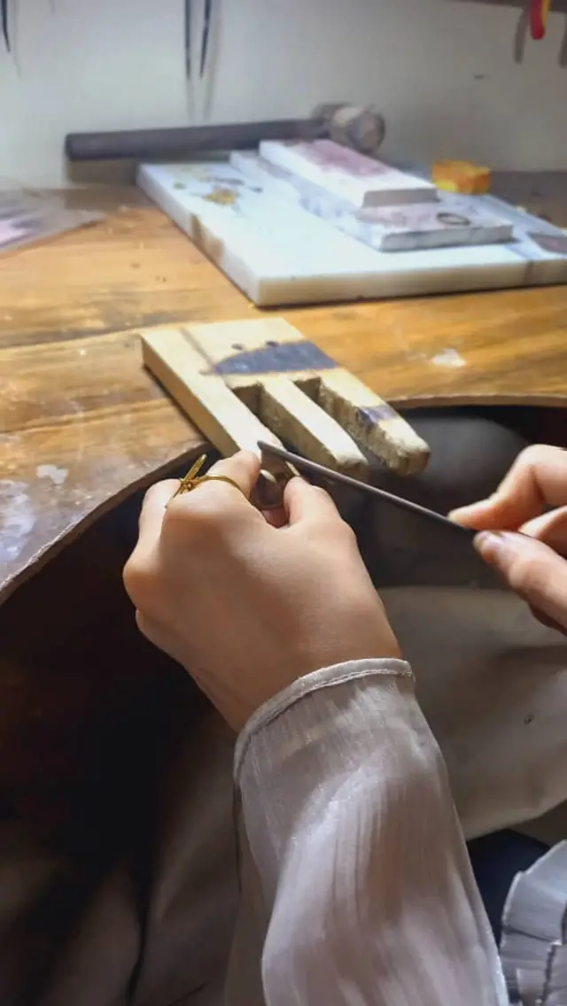 A woman, her face not shown, making jewelery at a desk