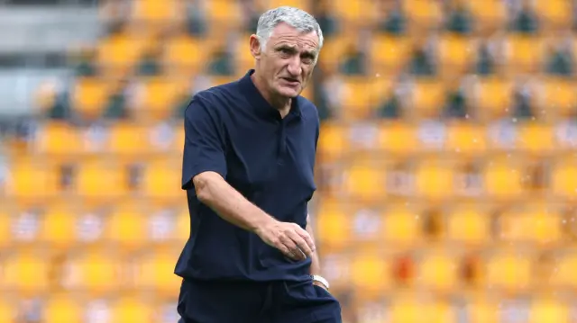 Tony Mowbray, wearing a navy blue polo shirt, walks on the pitch at Molineux before Blackburn's game against Wolves