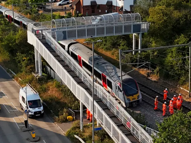 A closer up drone image showing railway workers assessing the train and railway tracks