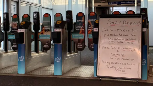 A whiteboard in front of closed railway gates. It says there has been an incident and all services are cancelled until further notice.