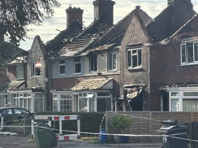 A row of five to six houses sit nearly completely destroyed and vacant. Windows are blown out and roofs have partially collapsed.