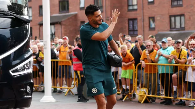 Wolves striker Raul Jimenez, wearing a teal green training shirt and shorts, arrives at Molineux and waves to the Wolves fans who can be seen clapping in the background