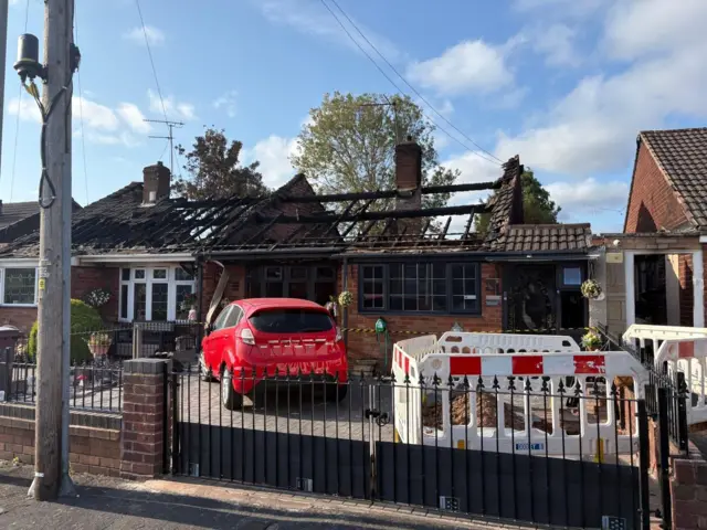 Two bungalows have their roofs completely burnt away. in the driveway of one, which has blackened windows, is a red Ford Fiesta
