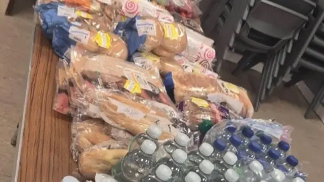 A table with lots of food, snacks and bottles of water