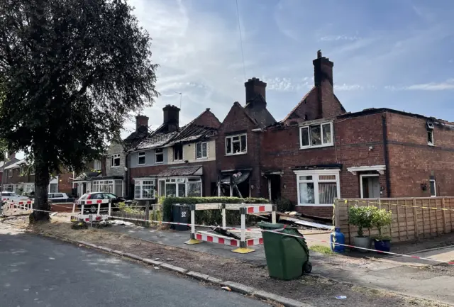 A row of houses cordoned off, with their roofs all destroyed from a fire