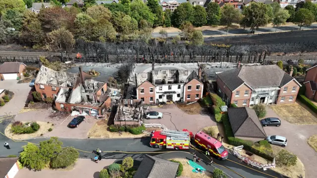 Drone footage of houses devastated in a fire, with roofs removed and walls burned down