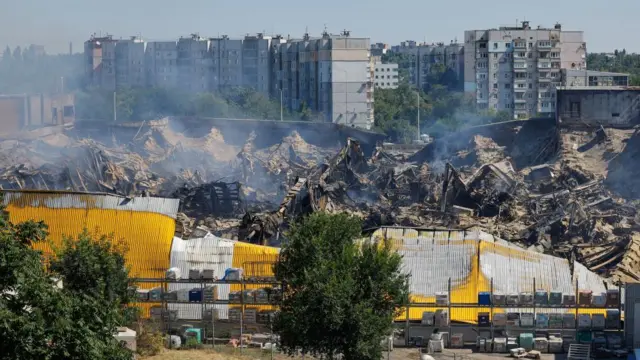 Burnt-out hypermarket smouldering and lying in rubble in front of lots of apartment blocks