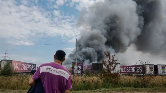 A Wildberries employee looks on as thick plumes of smoke rise behind several lorries with the company's branding