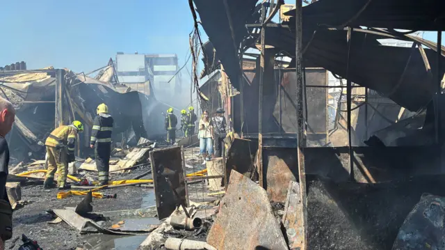 Firefighters work in front of shattered corrugated iron following a strike