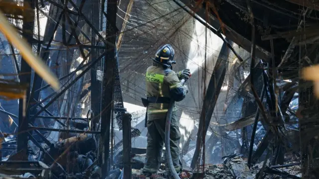 A firefighter works inside the ruins spraying a large hose
