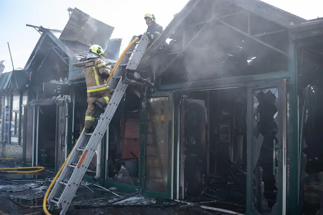 Firefighters climb a ladder at a stall in the heavily damaged market. The windows are shattered and the building is completely charred