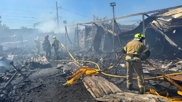 Firefighters carry several yellow hoses across the charred ground following an attack in Kyiv