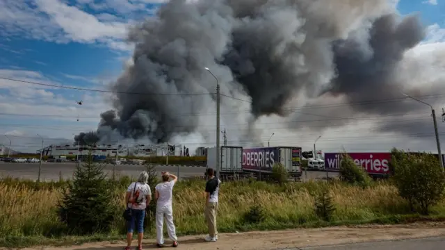 People watch as smoke rises above a Wildberries facility following a reported Ukrainian drone strike at the Koledino Industrial Park near Podolsk