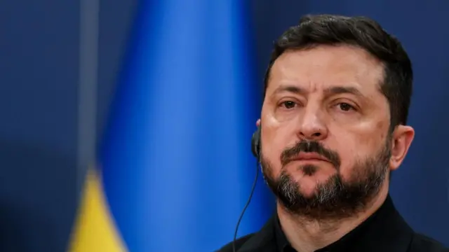 Ukrainian President Volodymyr Zelensky looks stern as he stands in front of a Ukrainian flag