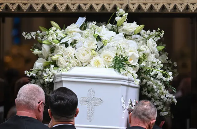 People carrying a white coffin with white flowers on top