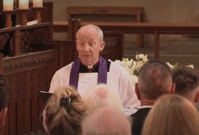 A man in purple and white speaks at the front of a church