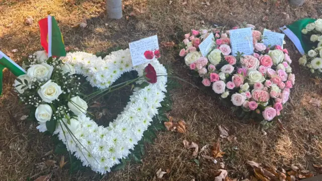 Floral tributes in the shape of love hearts are on the ground