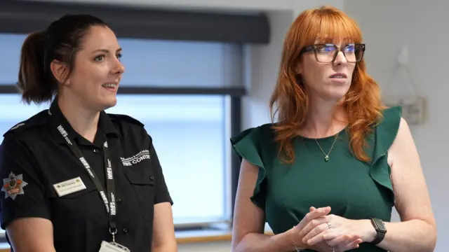 Angela Rayner, wearing a green dress, stands next to another woman with a black West Midlands Fire Service shirt.