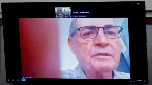 Fred Miller on a Zoom call wearing glasses. His finger partially covers the lens of his camera.